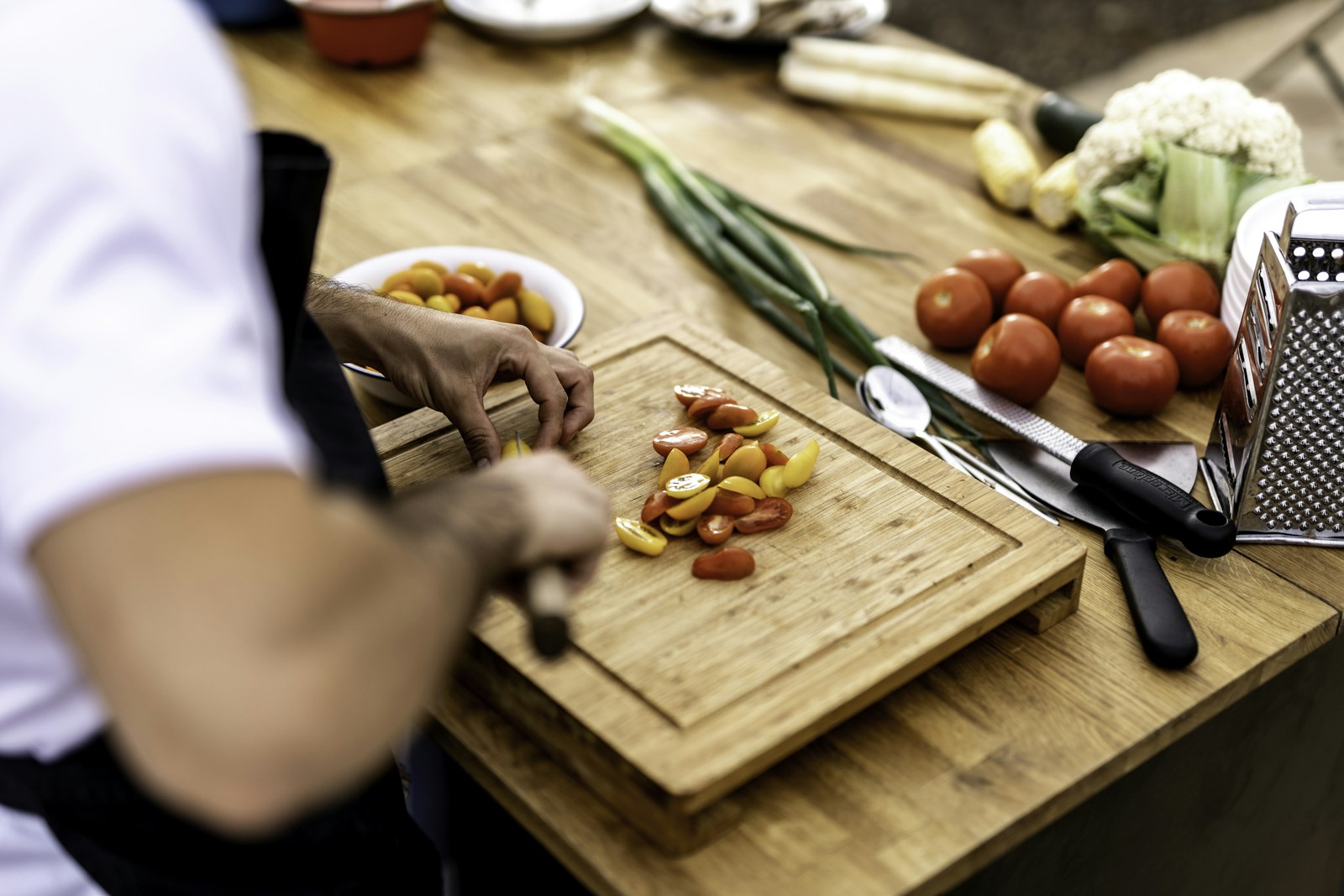 A chef slicing fresh tomatoes on a wooden chopping board, with vegetables ready for preparation